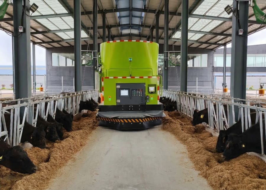 An integrated farm system showing a TMR mixer, a feed spreader, and a manure scraper in action