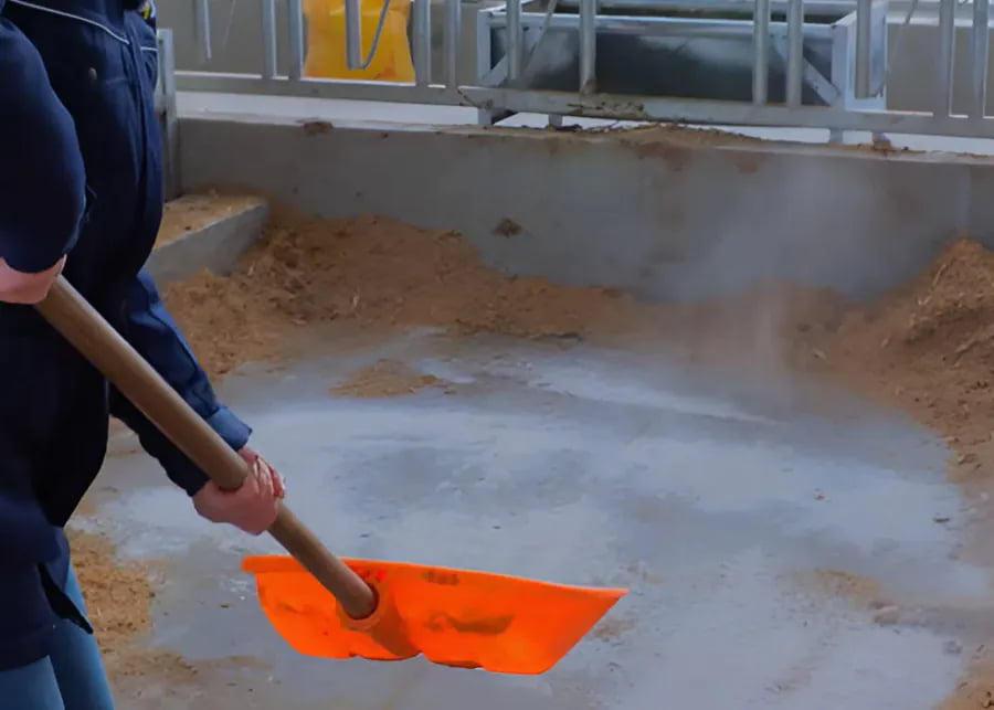 A worker spreading a thin layer of quicklime powder on a concrete floor.