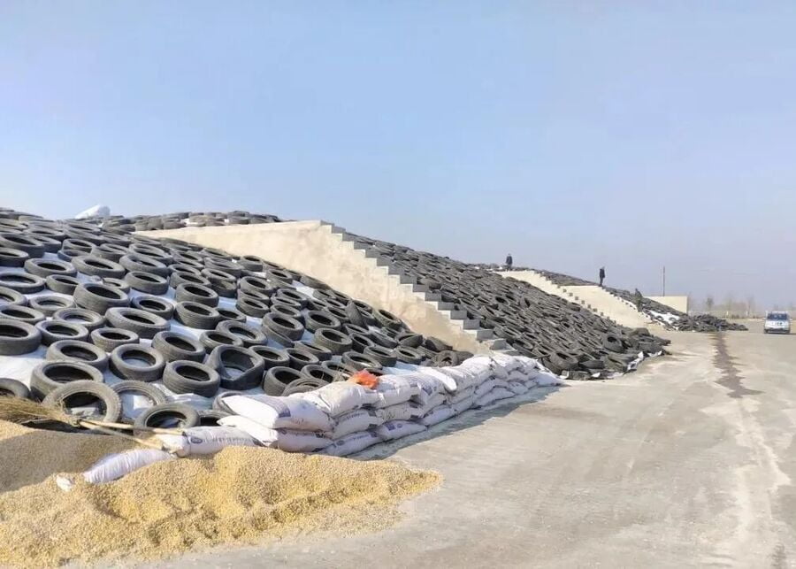 A massive multi-bunker silo facility sealed with plastic sheets, tires, and edge-weighting sandbags