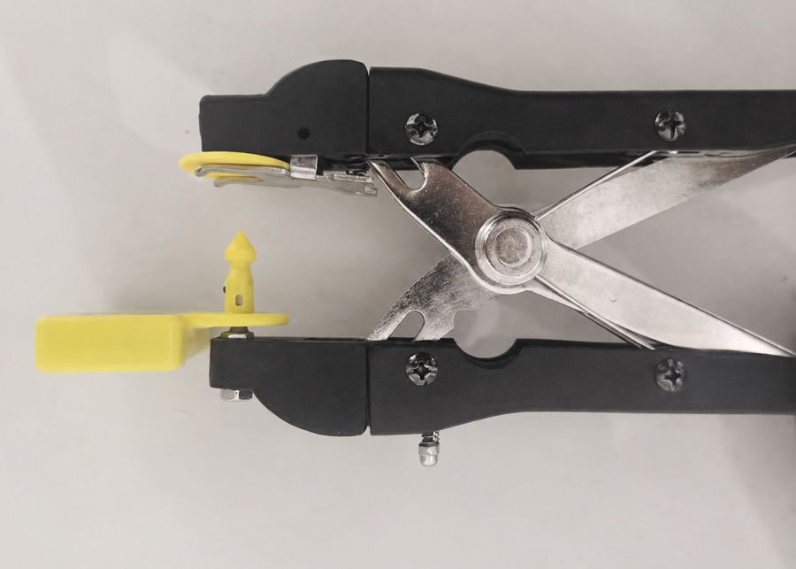 Close-up of a heavy-duty ear tag applicator properly loaded with a thick smart cattle sensor tag and special pin