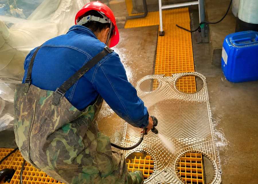 Technician using a high-pressure water jet to clean milkstone from a disassembled plate heat exchanger plate