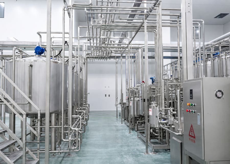 A clean and well-ventilated dairy processing facility featuring structured stainless steel pipelines and enclosed control panels protected from corrosive vapors.