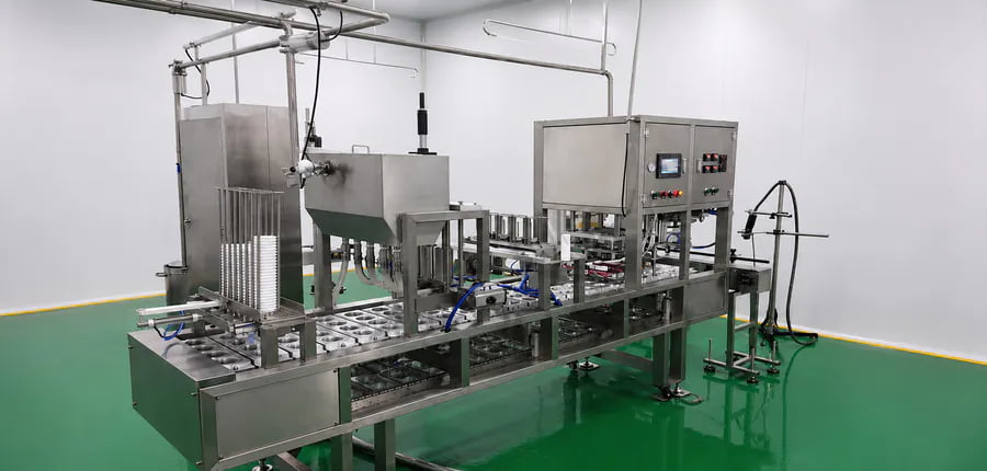 Automatic linear yogurt cup filling and foil sealing machine with cup dispenser in a cleanroom facility