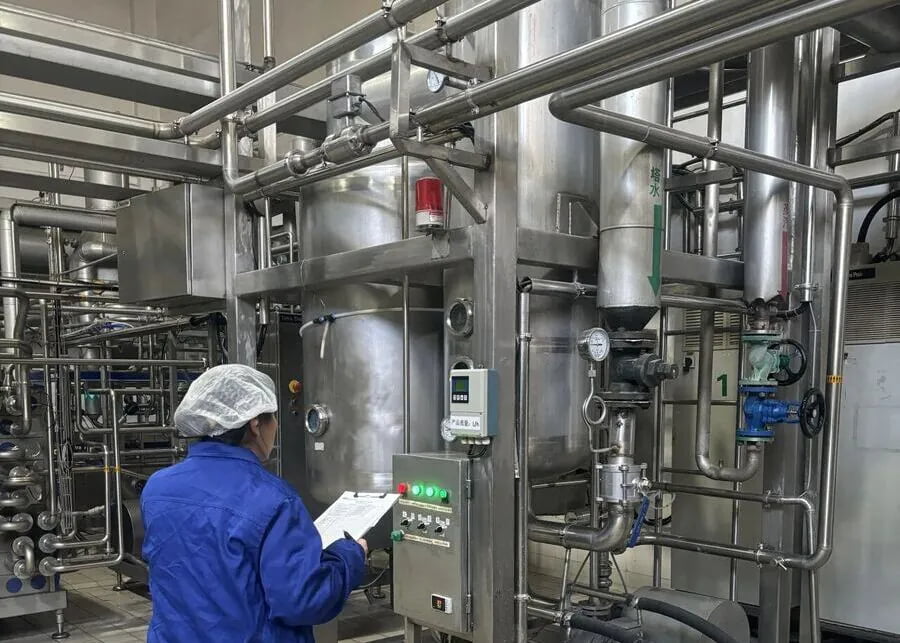 Dairy plant operator monitoring CIP cleaning parameters and complex stainless steel piping system for biofilm removal