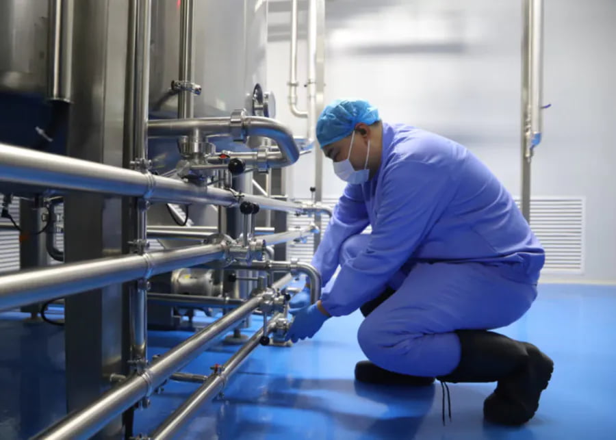 Dairy plant technician inspecting stainless steel piping system for proactive biofilm prevention