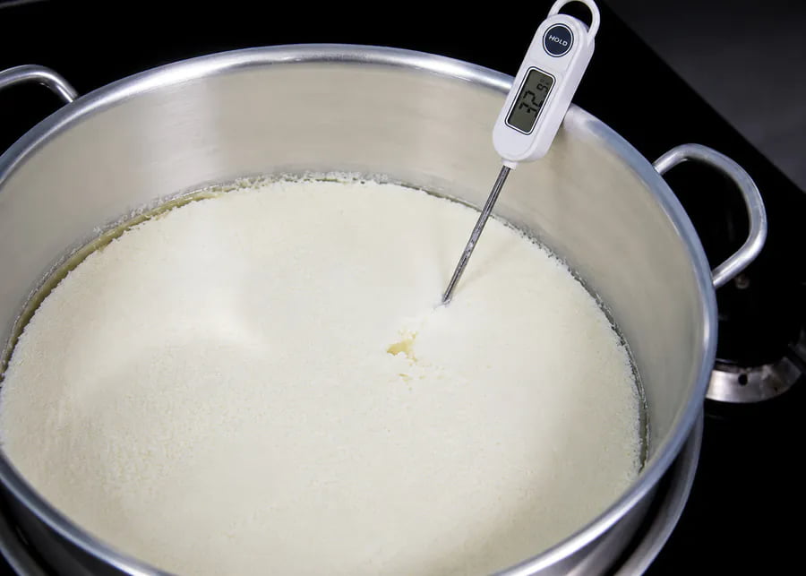 A digital thermometer measuring the precise temperature of milk in a stainless steel pot to prevent bitter homemade yogurt.