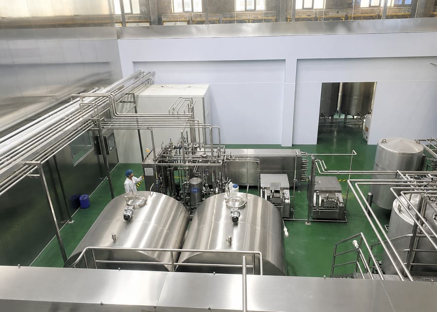 Turnkey Dairy Processing Plant Utilities and Piping Manifolds Overhead view of an integrated turnkey dairy production line featuring horizontal storage tanks, stainless steel piping manifolds, and a plate pasteurizer skid