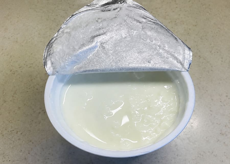 Close-up of yogurt cup demonstrating syneresis (whey separation) on the surface, indicating an unstable protein gel matrix.